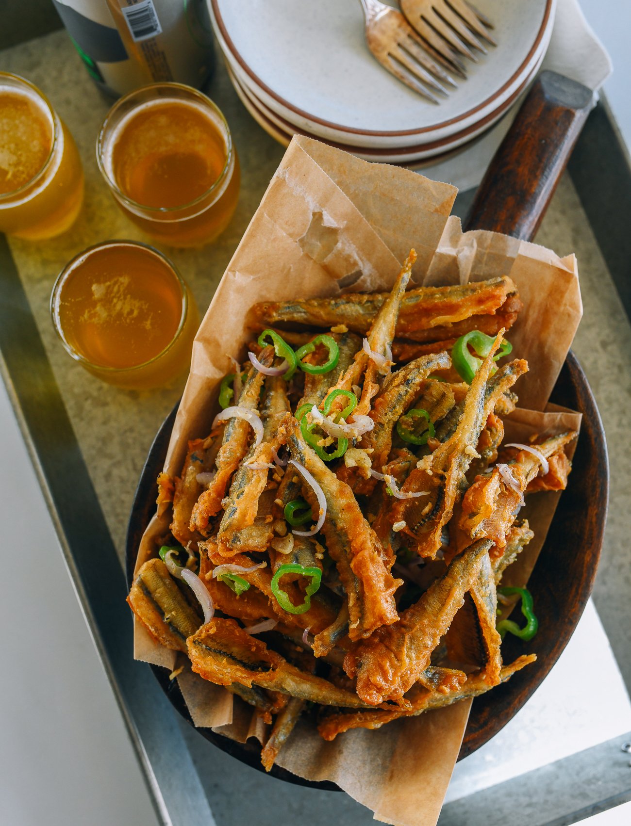 Basked of Salt and Pepper Fried Smelts on table next to three glass of what appears to be beer