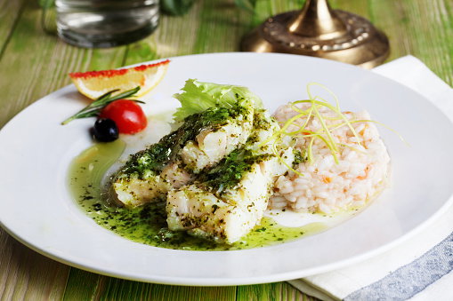 White fish in topped with green sauce in white place