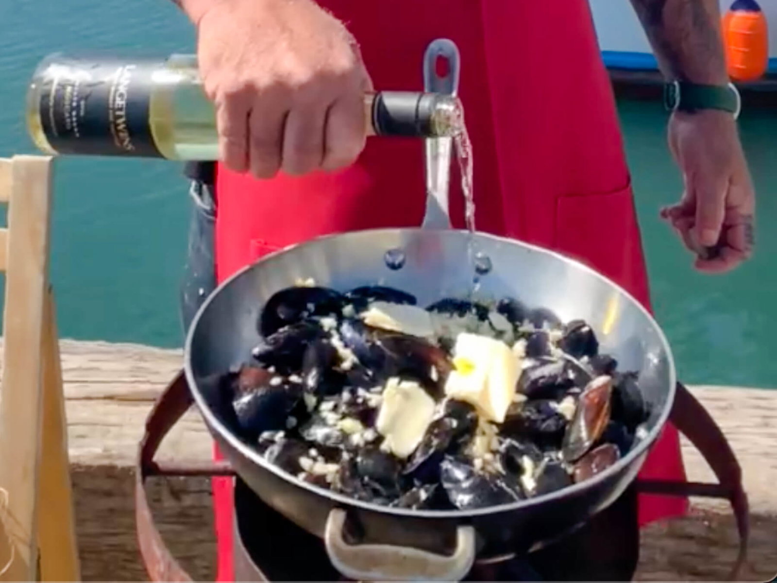 Hans pouring white wine into a pan filled with Mussels, butter, and shallots