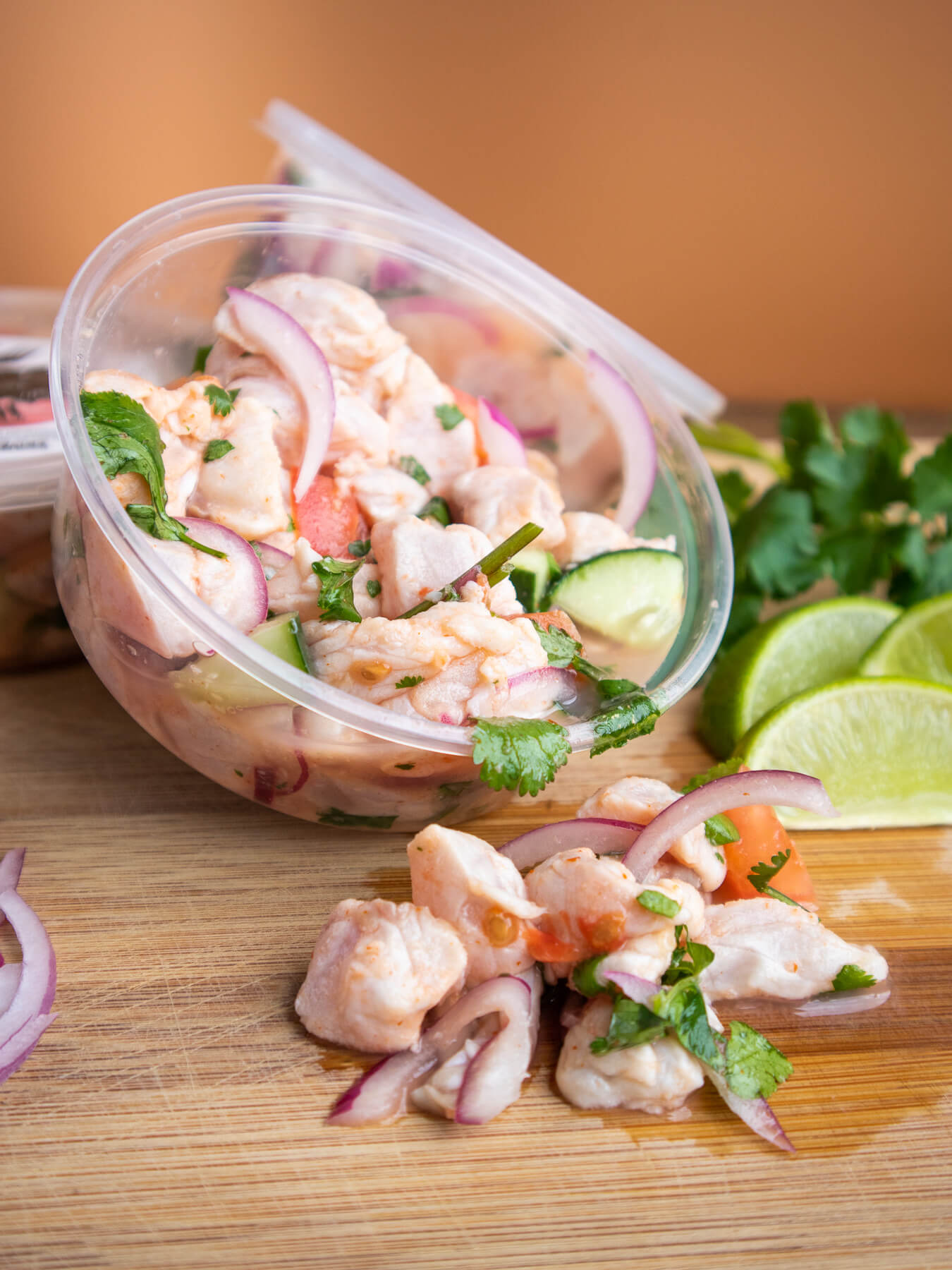 Three clear containers of Rockfish Ceviche (one container is opened opened) on cutting board with fresh herbs and other ingredients