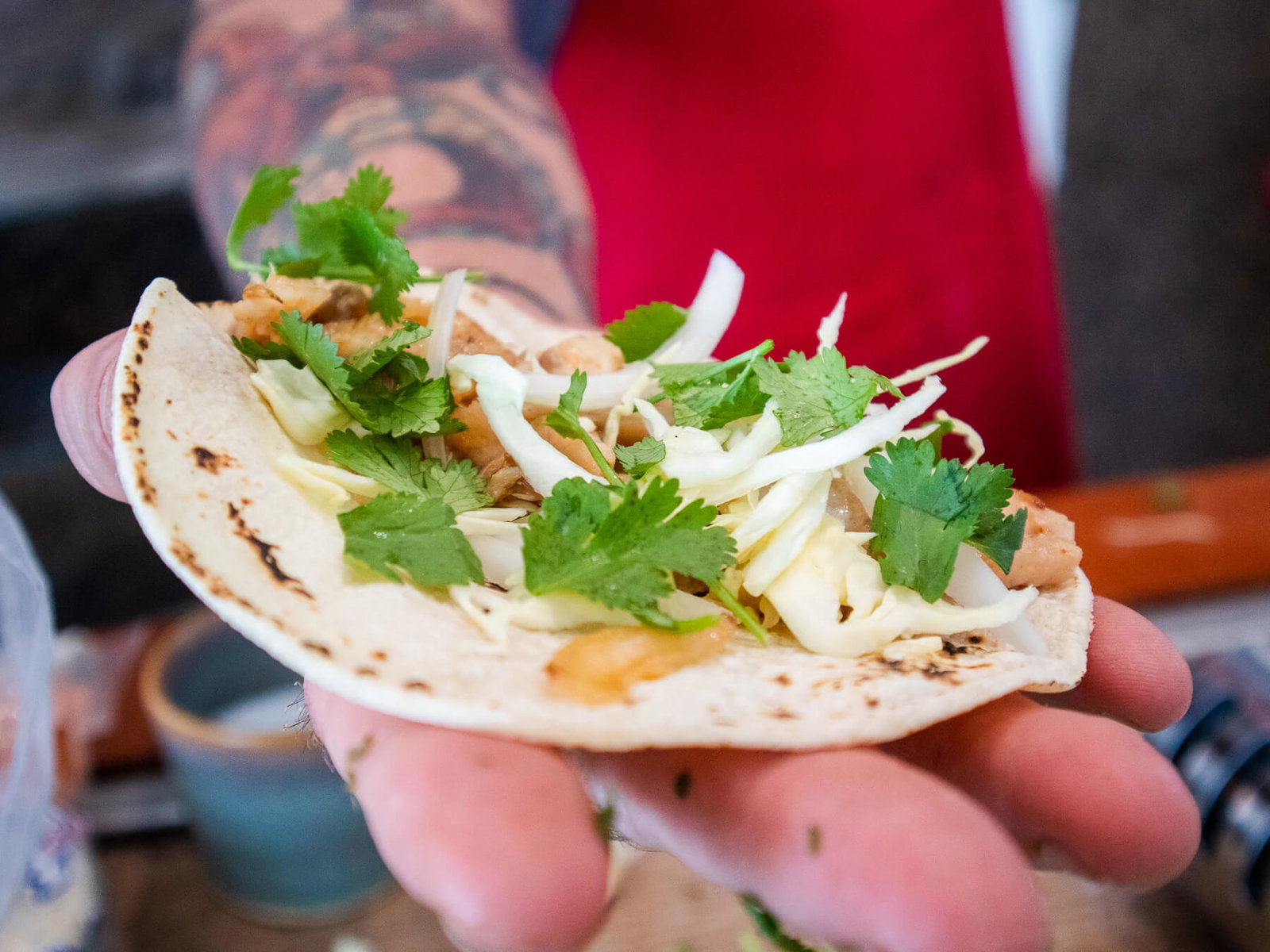 Hans (wearing a red apron, glasses, and gray H&H Fresh Fish hat) eating a Rockfish taco