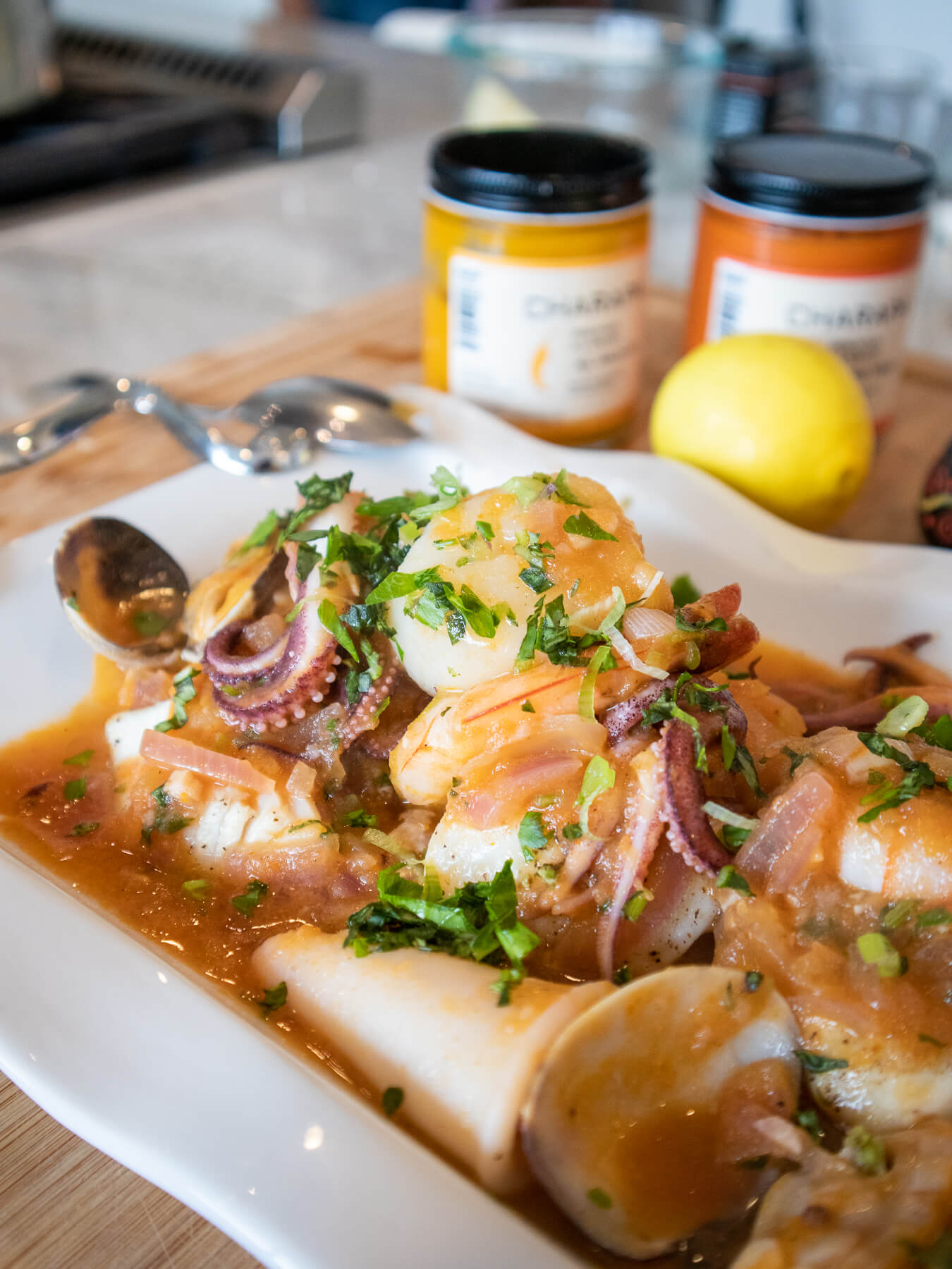 Pescado a lo Macho, a traditional Peruvian seafood dish with squid and mussels in a spicy pepper sauce, garnished with herbs, accompanied by Charapa sauce jars and a lemon.